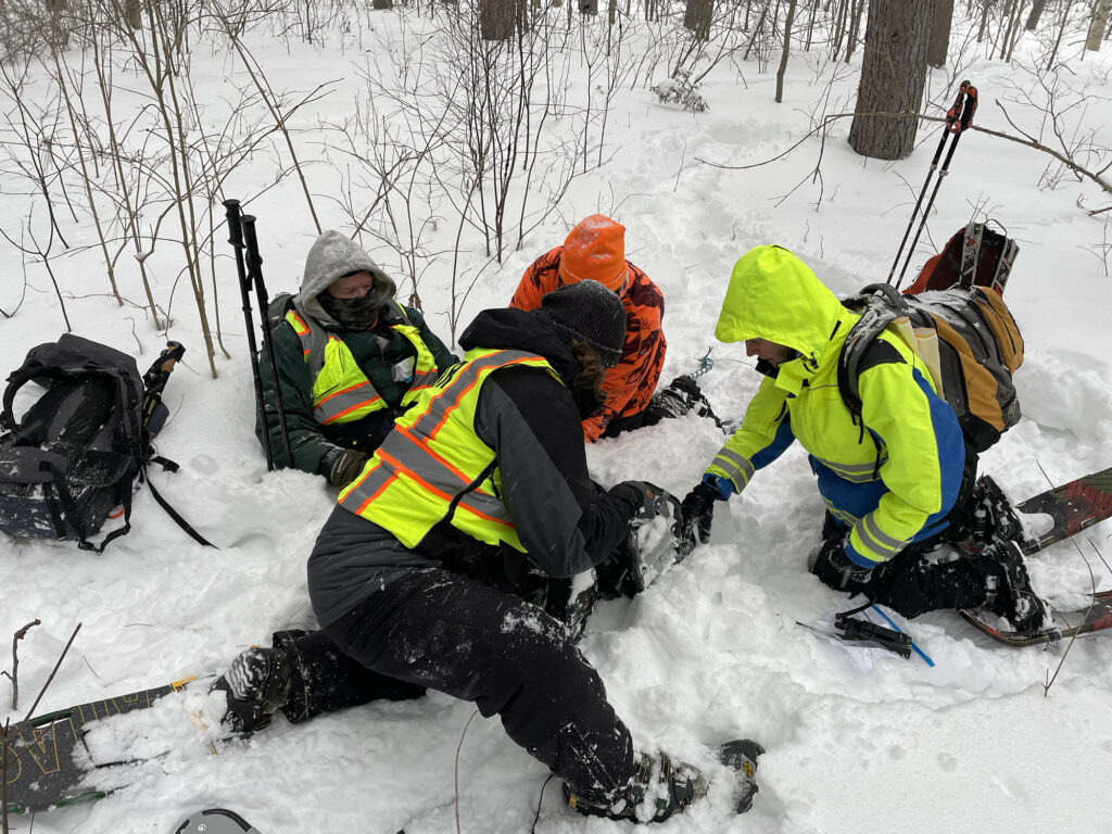 SAR volunteers assess an a mock injury in a snowy forest.