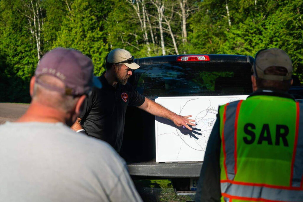 Patrick Diedrich discusess search details on a whiteboard resting on the bed of his truck.