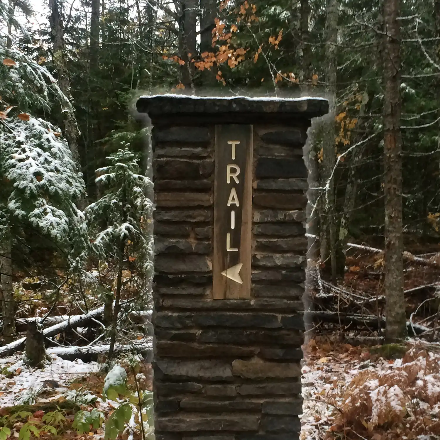 Photo of a trail marker with a snowy autumn forest in the background.